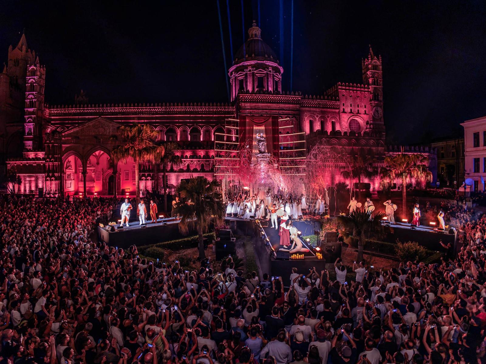 Palermo Cathedral lit in red during the Festino di Santa Rosalia, with performers on stage before a large crowd